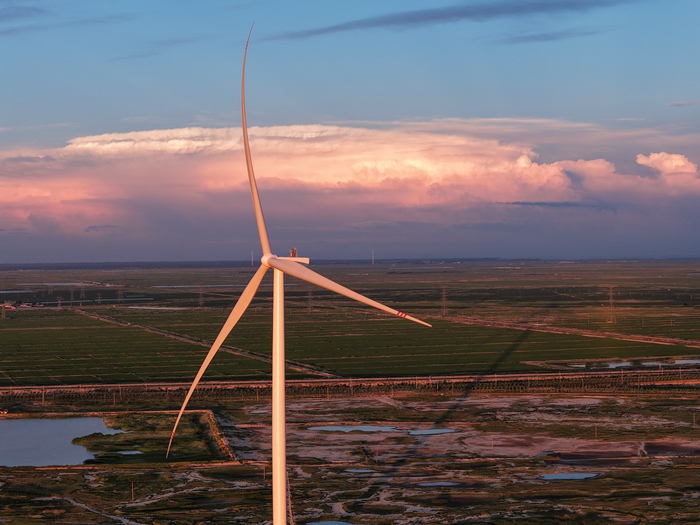 夕陽下,一臺臺風(fēng)機(jī)在風(fēng)中源源不斷地產(chǎn)生電能。吉電股份供圖